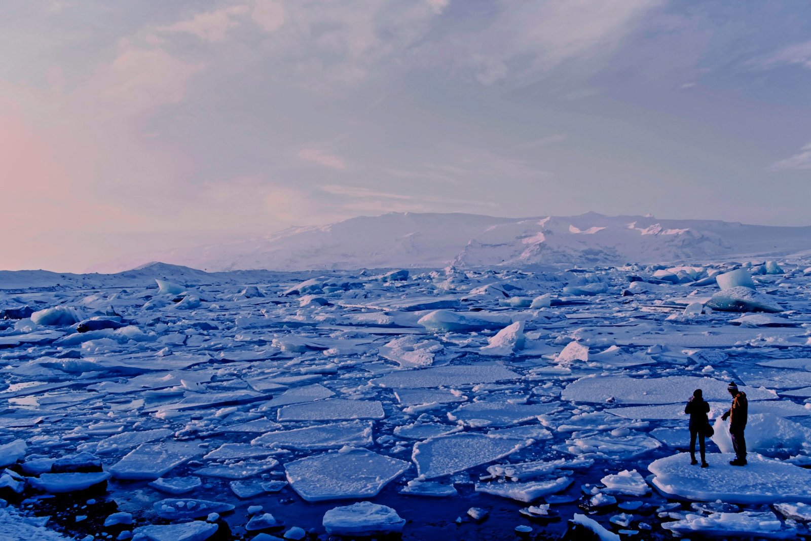 man and woman standing cracked sea ice under gray sky